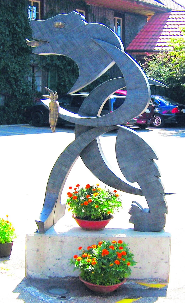 Metallskulptur eines Bären mit Blumenschmuck davor