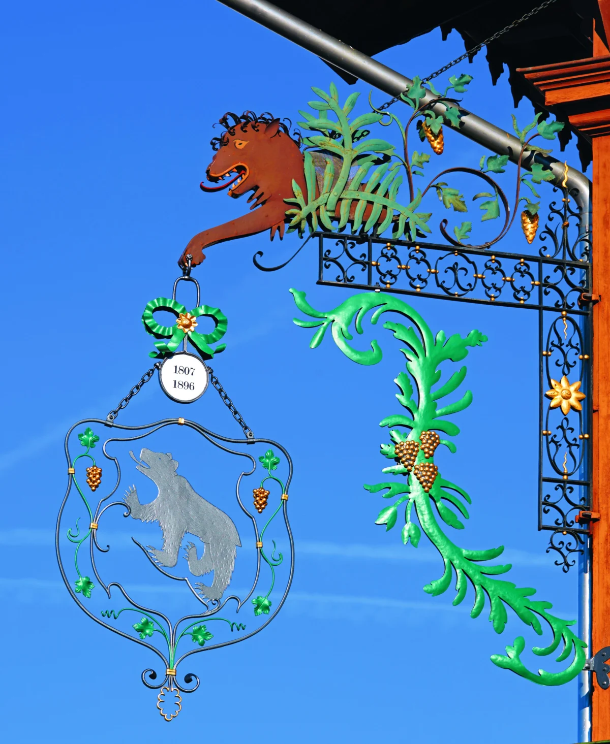 Wirtshausschild mit Bärenwappen und grünen Verzierungen vor blauem Himmel