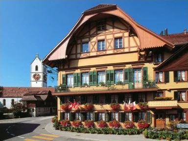 Landgasthof Bären in Sumiswald, Fachwerkhaus mit Blumenkasten und Kirchturm im Hintergrund